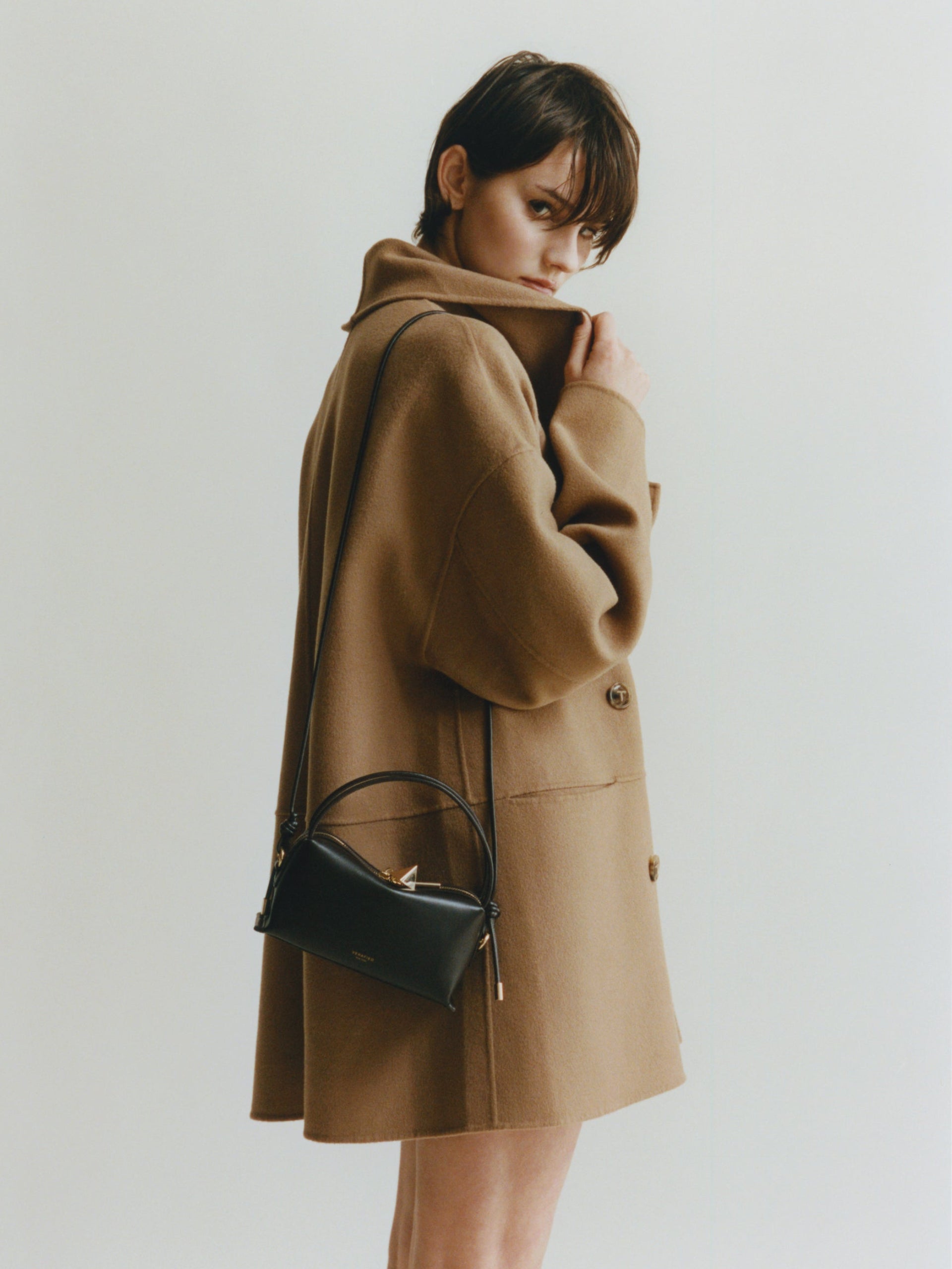 Person wearing a brown coat holding a Chocolate Café Mini Crossbody Handbag against a plain background