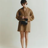 Person wearing a brown coat and skirt holding a Chocolate Café Mini Crossbody Handbag on a plain background