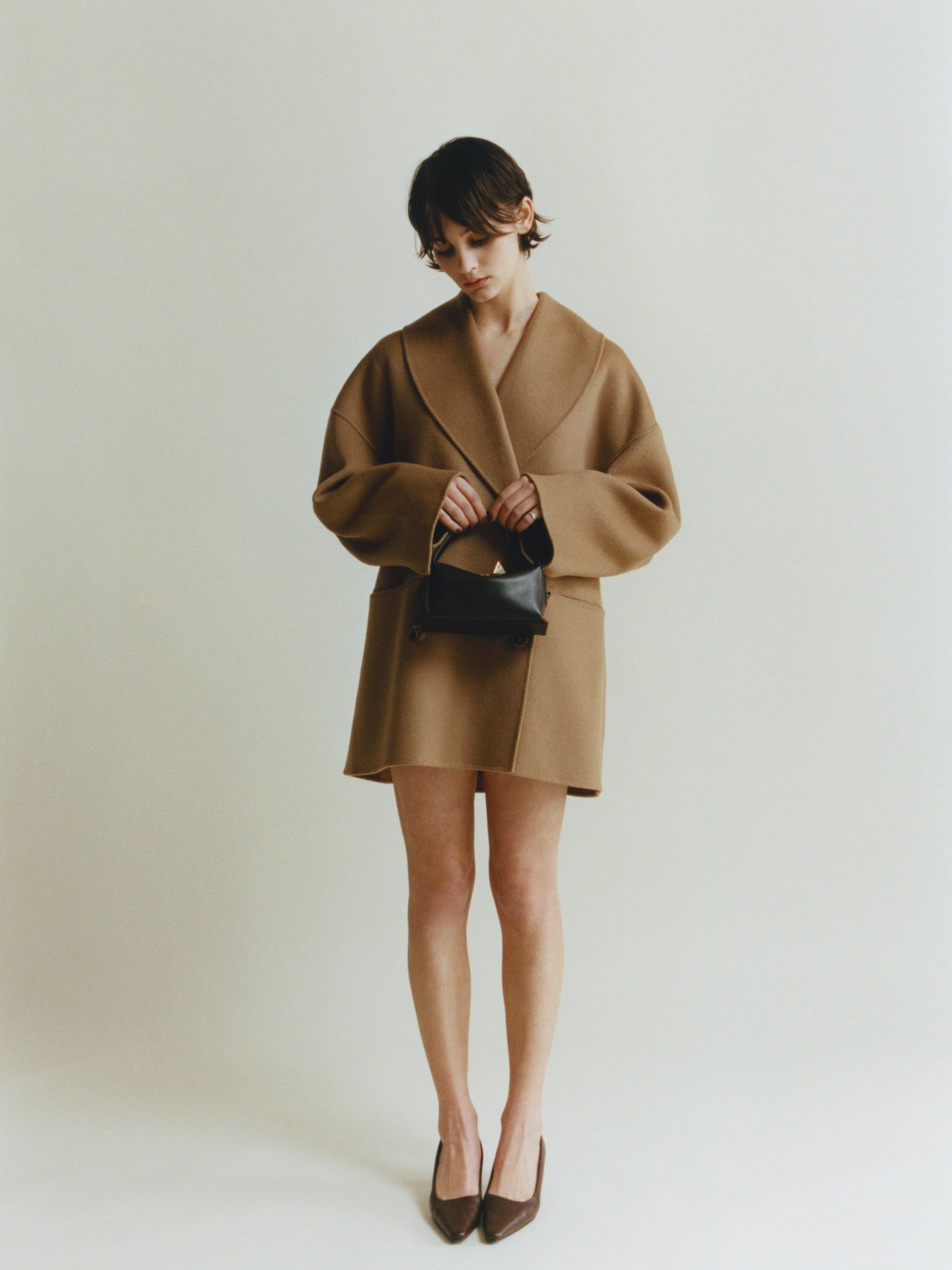 Person wearing a brown coat and skirt holding a Chocolate Café Mini Crossbody Handbag on a plain background