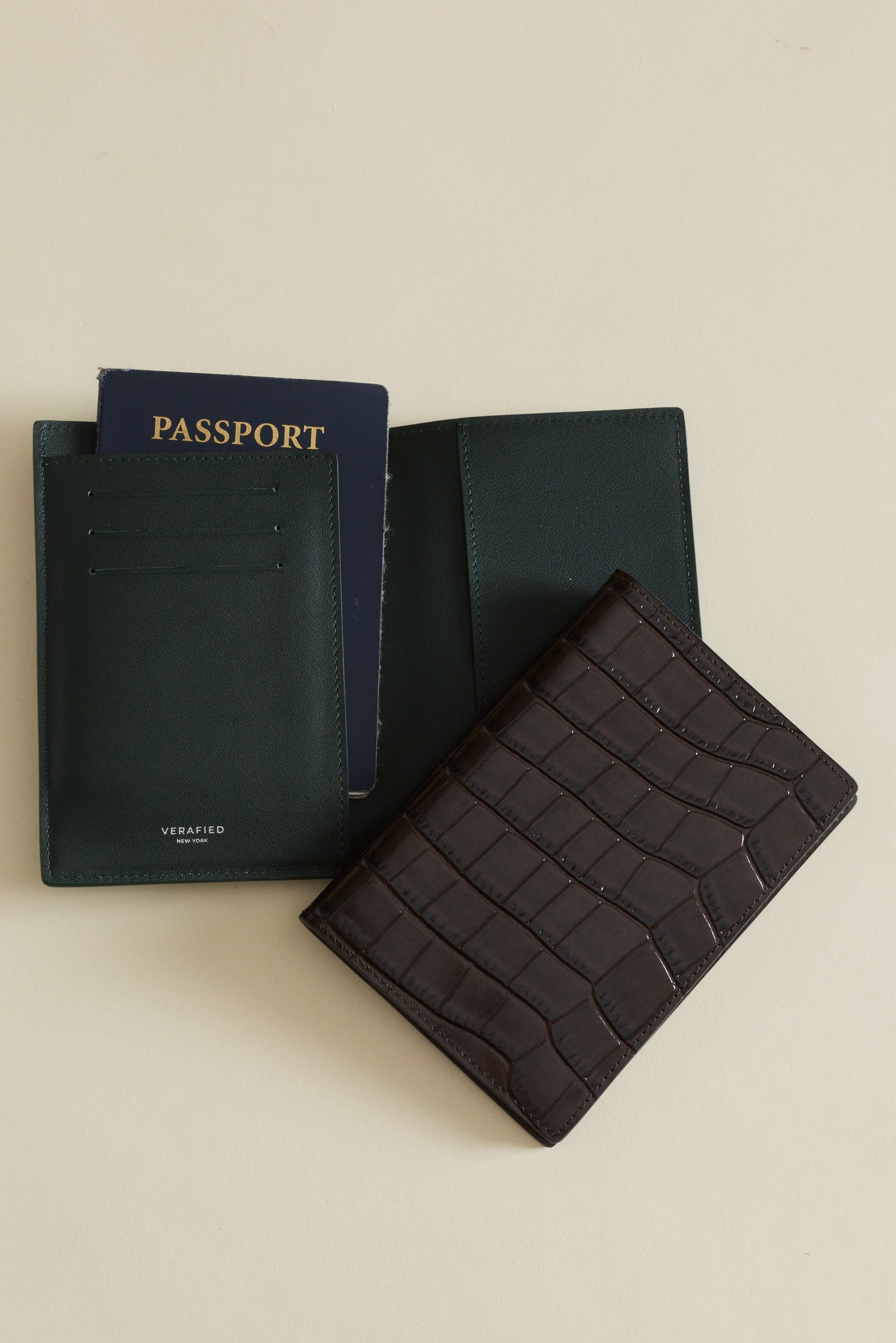 Black passport holder with a passport and Mocha Croc Embossed Passport Cover Wallet on a beige background