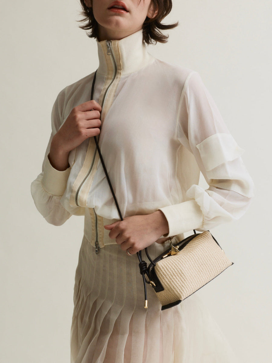 Person wearing a white blouse with a beige jacket and holding a matching Raffia Café Mini Crossbody Handbag against a neutral background