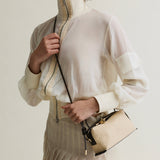 Person wearing a white blouse with a beige jacket and holding a matching Raffia Café Mini Crossbody Handbag against a neutral background