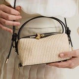 Beige Raffia Café Mini Crossbody Handbag with black straps held by a person wearing a white dress.