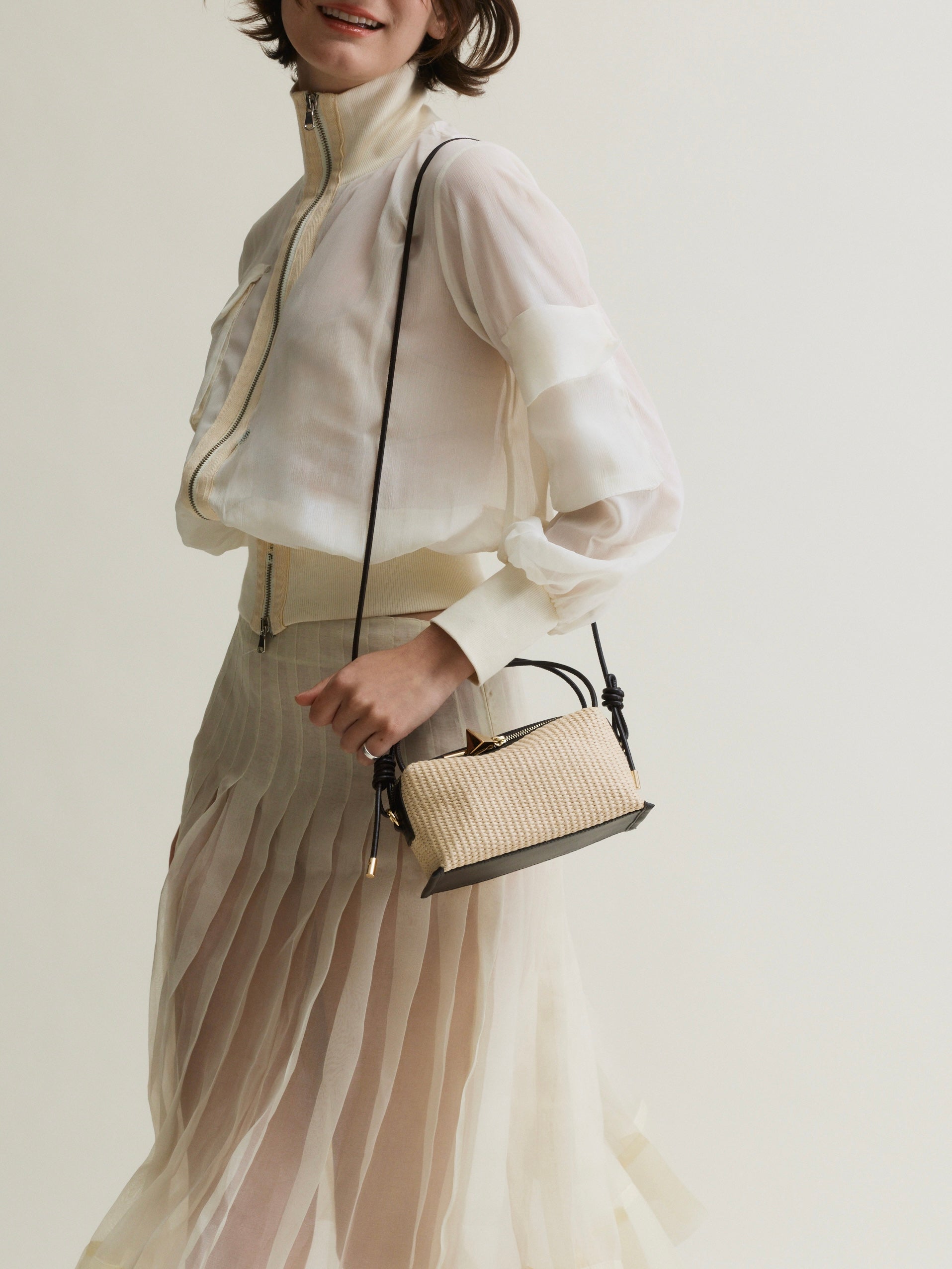 Woman holding a Raffia Café Mini Crossbody Handbag against a plain background
