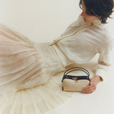 Woman in a white dress holding a Raffia Café Mini Crossbody Handbag against a plain background