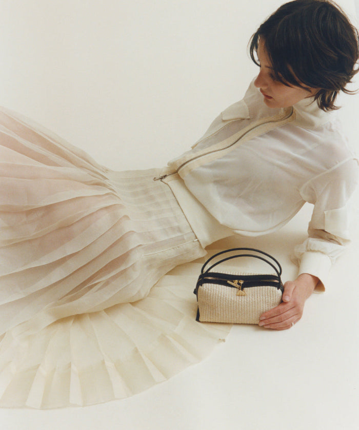 Woman in a white dress holding a Raffia Café Mini Crossbody Handbag against a plain background