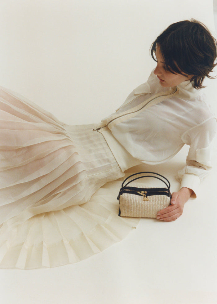 Woman in a white dress holding a Raffia Café Mini Crossbody Handbag against a plain background