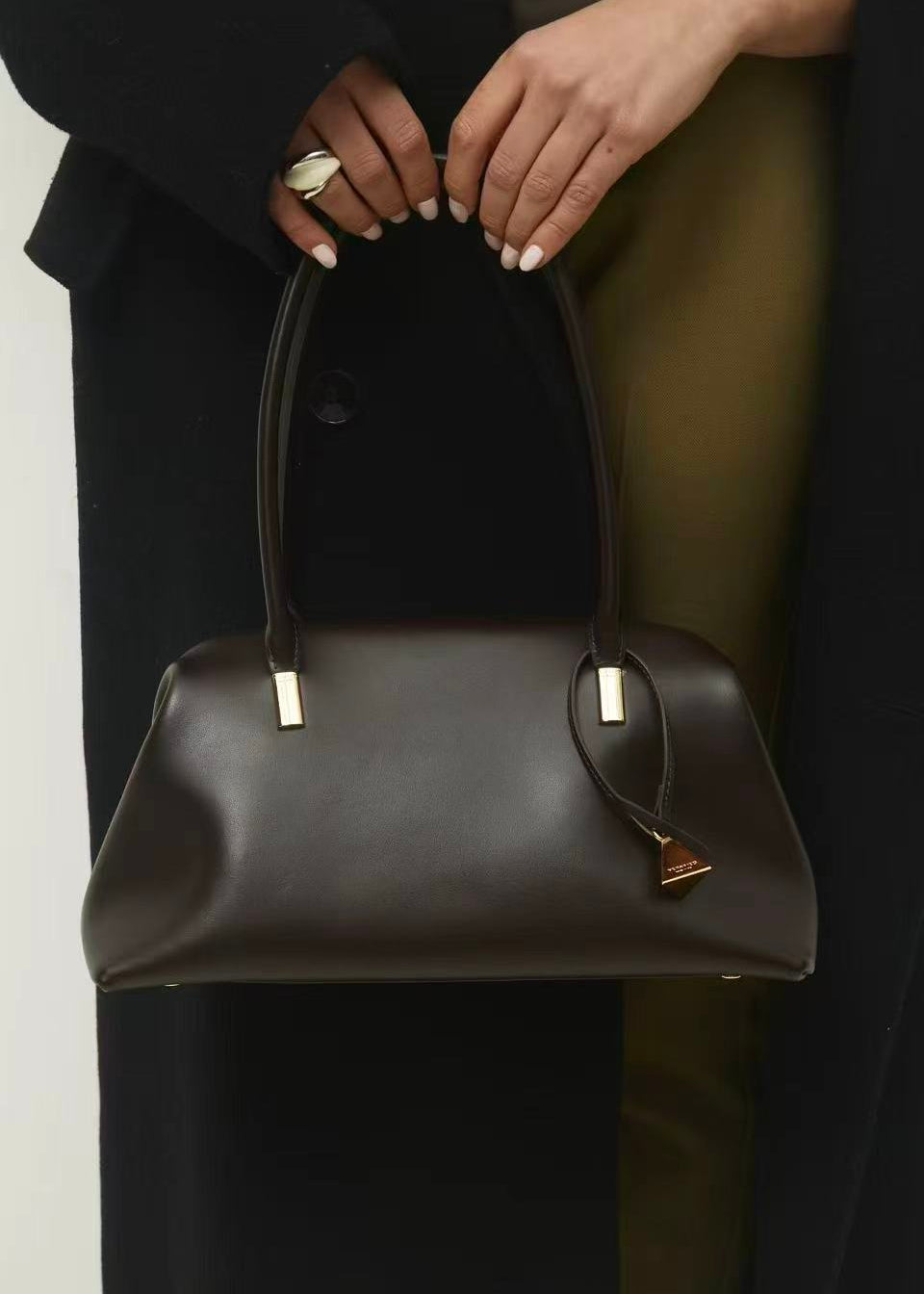 Person holding a Chocolate Medium Club Shoulder Handbag with gold accents against a neutral background