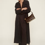 Woman in a long black coat holding a brown hobo bag against a white background