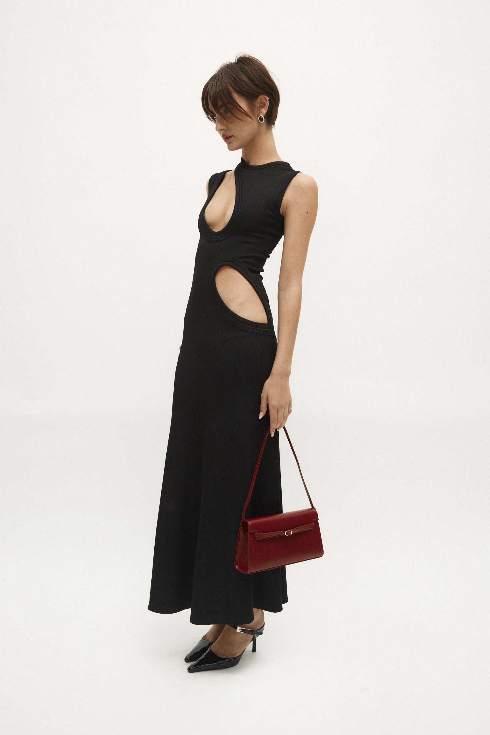 Woman wearing a black dress with cut-out design, holding a Dark Cherry Shoulder Purse Handbag on a white background