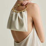 Woman wearing a white dress with a Cream Circle Ring Handle Bag on her shoulder against a neutral background