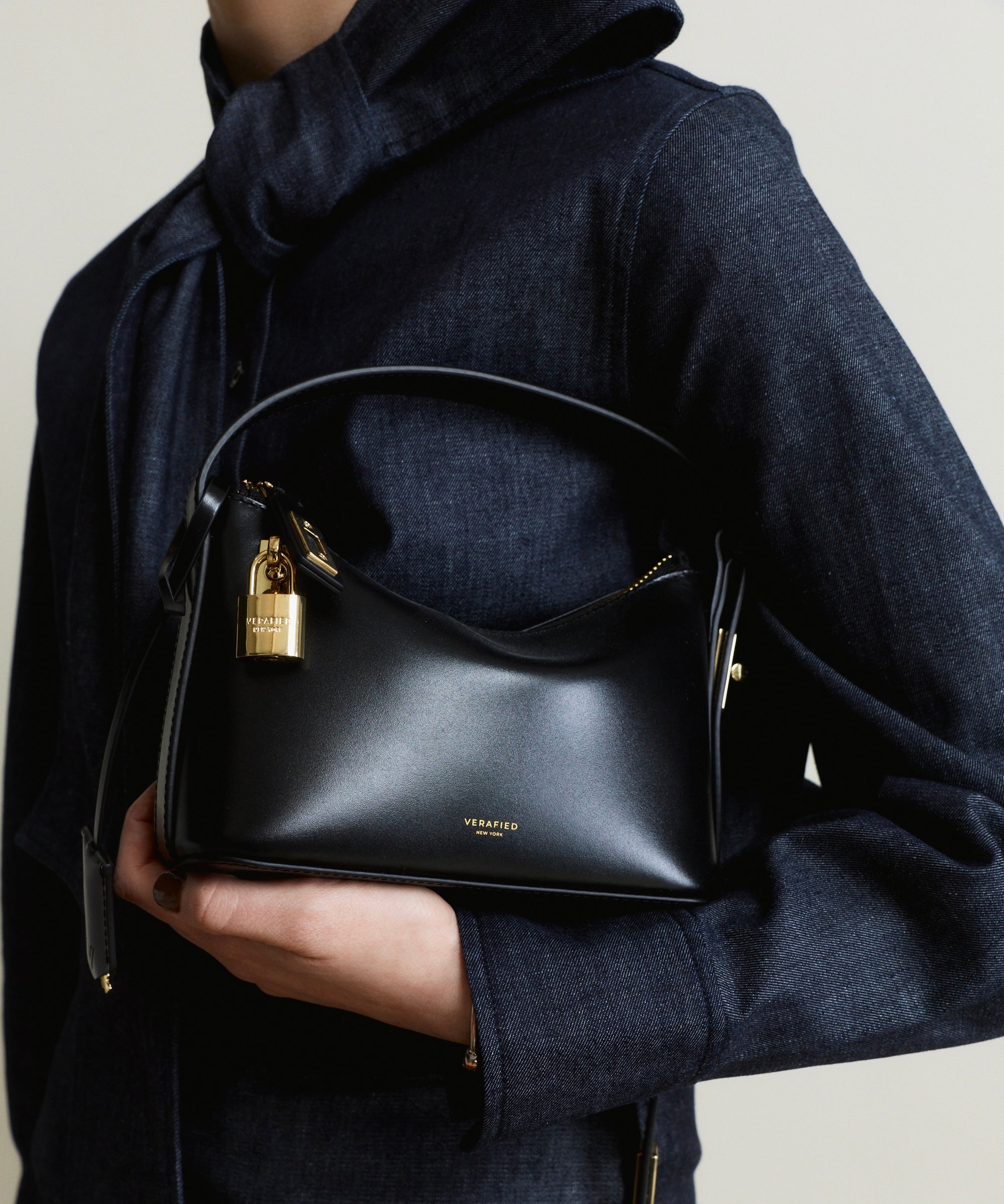 Person holding a Mini Gold Black Hobo Shoulder Handbag with a gold lock, wearing a dark coat.