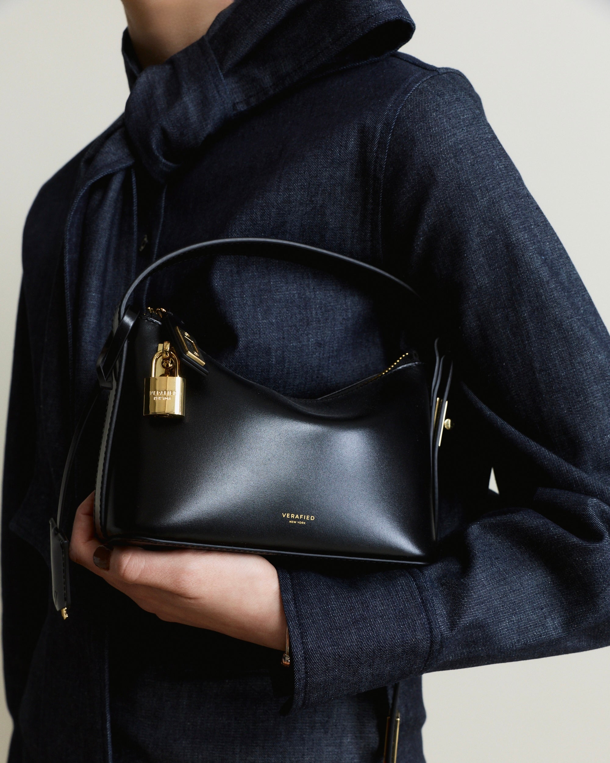Person holding a Mini Gold Black Hobo Shoulder Handbag with a gold lock, wearing a dark coat.