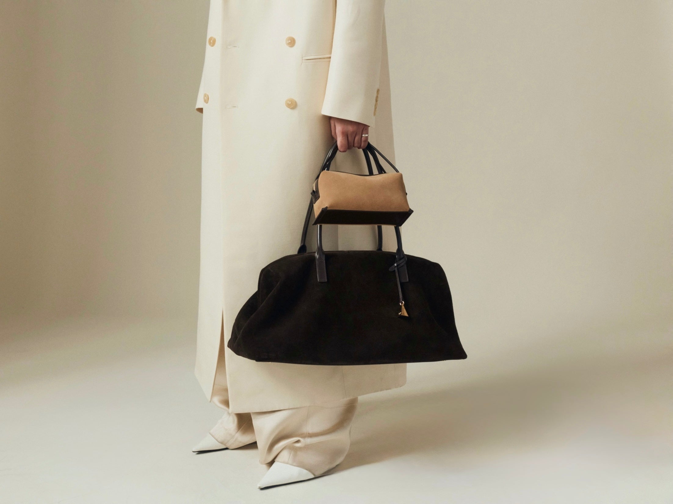 Person holding a black Verafied New New York handbag with a beige top handle against a neutral background