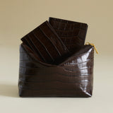 Brown crocodile-patterned clutch bag with a smaller Mocha Croc Embossed Passport Cover Wallet on a beige background