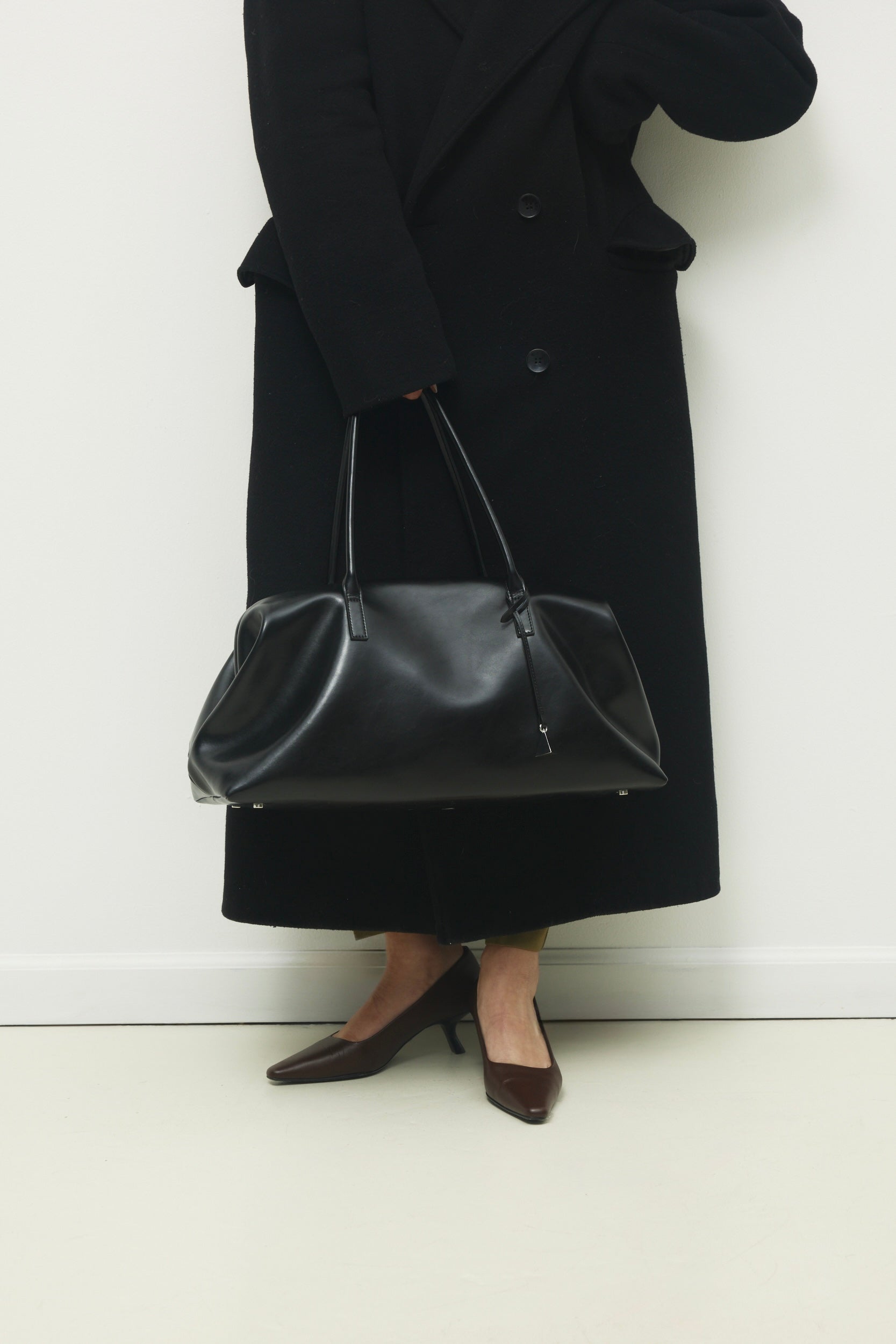 Person wearing a black coat and holding a Black Club Large Handbag against a white background