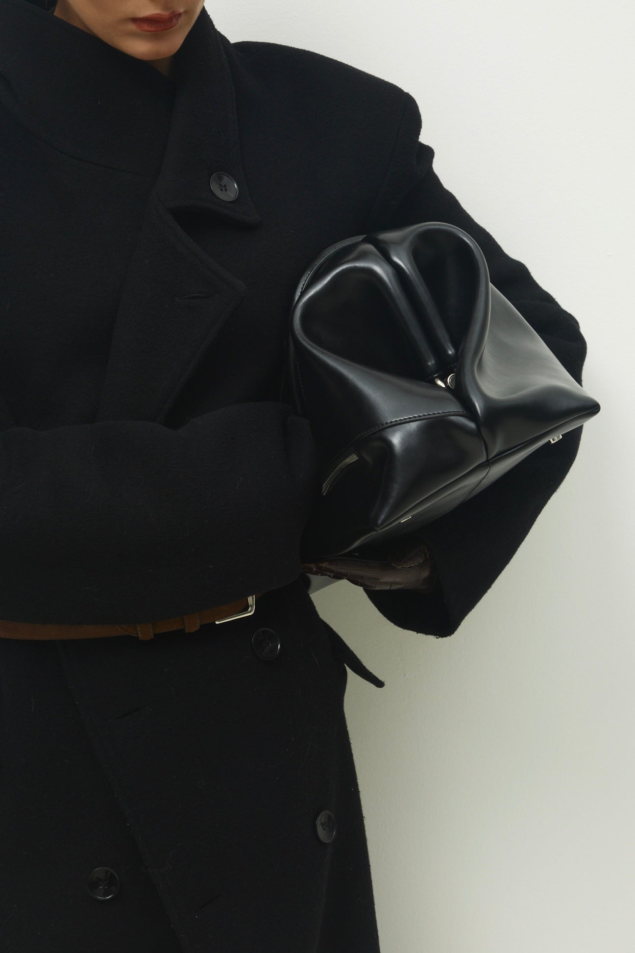 Person wearing a black coat holding a Black Club Large Handbag against a white background