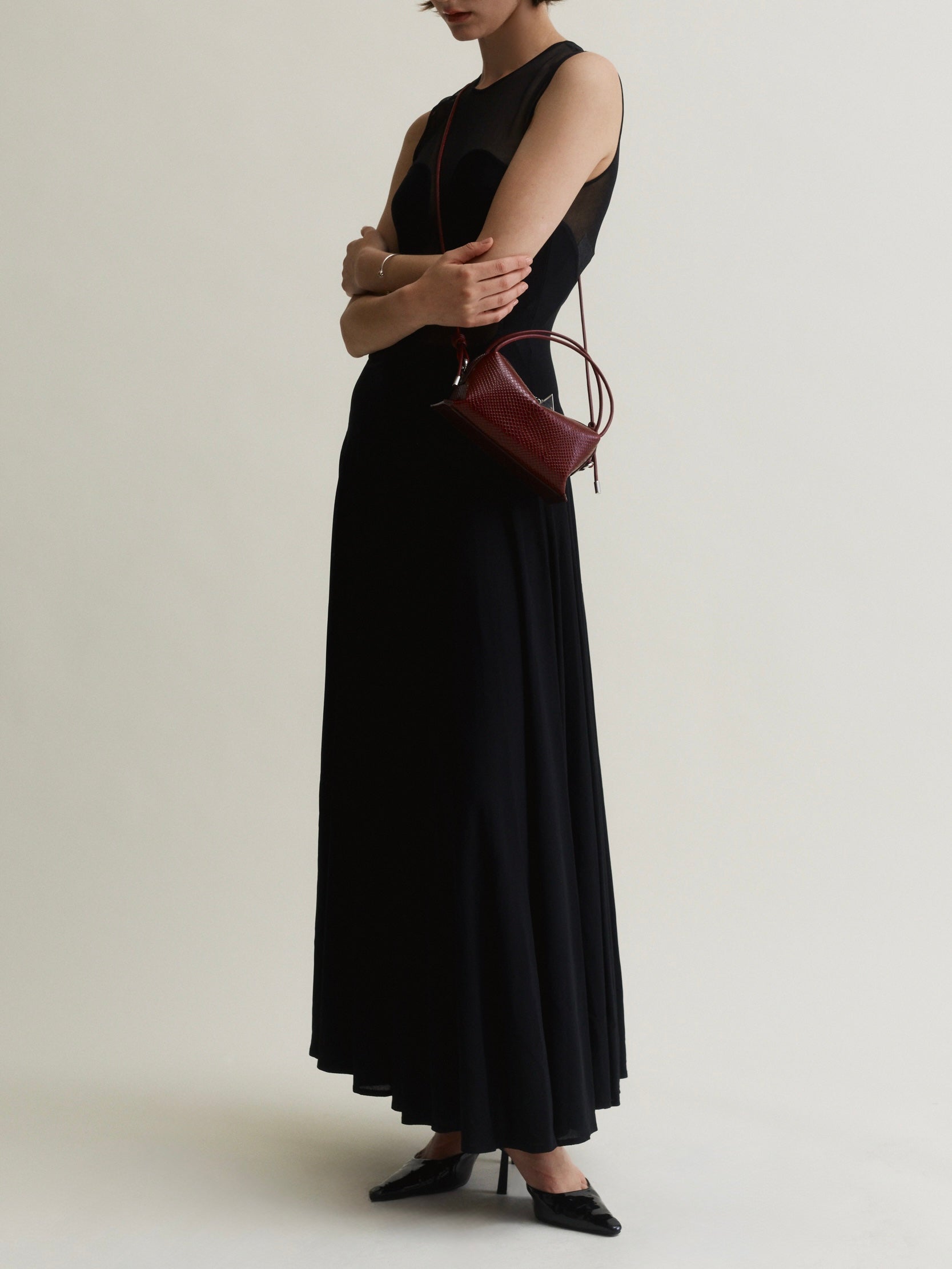 Person wearing a black dress holding a Maroon Python Café Mini Bag: Crossbody Handbag on a plain background
