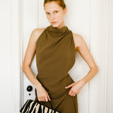 Woman in a brown dress holding a Zebra Calf Hair Éclair Shoulder Handbag against a white door.
